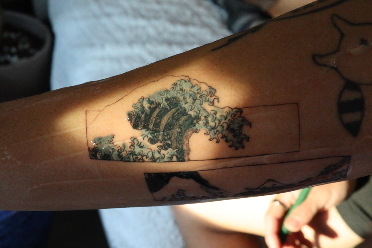 Black-and-grey great wave rendered inside a fine-line rectangular frame on the forearm